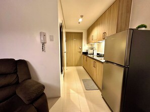 A narrow kitchen with wooden cabinets, a refrigerator, and a microwave. - Luxury Seaside Sunset View Mall of Asia with Free Parking (Pasay City)