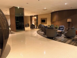 A modern lobby with a curved ceiling, a reception desk, and seating areas with upholstered chairs. - Luxury Seaside Sunset View Mall of Asia with Free Parking (Pasay City)