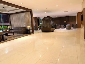 A modern hotel lobby with a sofa, armchairs, a coffee table, and a unique seating structure. - Luxury Seaside Sunset View Mall of Asia with Free Parking (Pasay City)