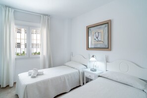 A hotel room with two beds, a window with curtains, a bedside table with a lamp, and a framed picture on the wall. - Villa in Nerja Near Burriana Beach (Nerja)