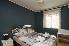 Ein Schlafzimmer mit einem Bett, einem Nachttisch, einer Lampe, einem Spiegel und einem Fenster mit Vorhängen.