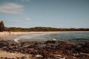 Una playa con un primer plano rocoso, orilla de arena y gente nadando.