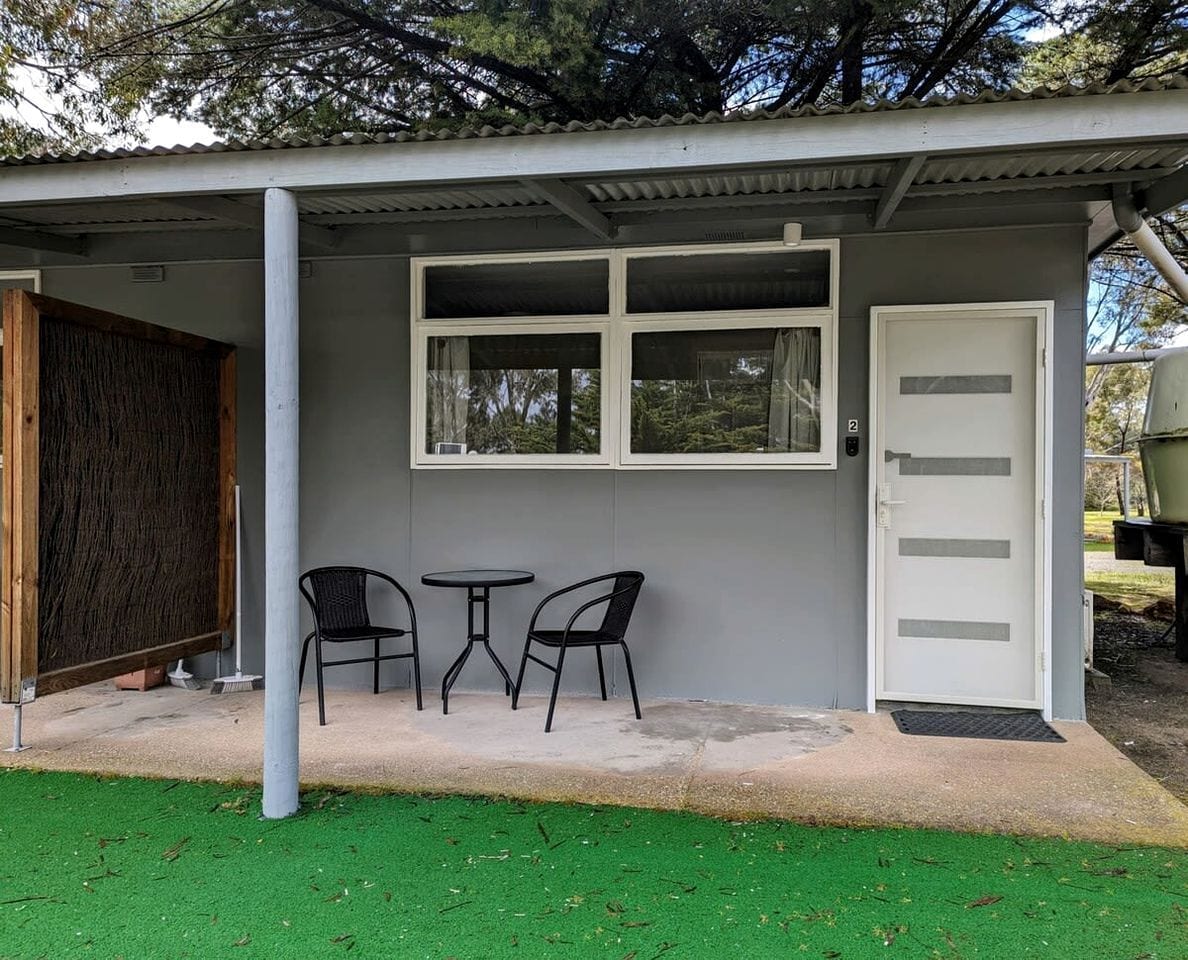 A small building with a covered patio area, a door, and two chairs.