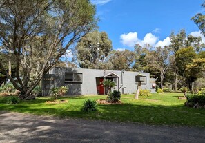 A modern two-story house with a red door, surrounded by a well-maintained garden and trees.