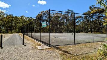 A fenced area with a gravel path leading to a parking lot, surrounded by trees.