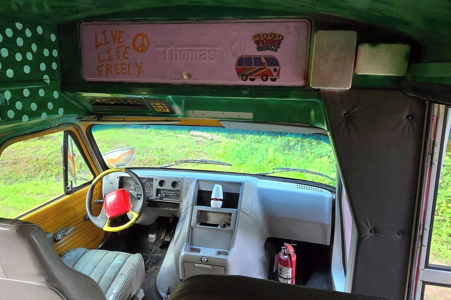 L'intérieur d'une voiture ancienne, avec un volant, un tableau de bord et une pancarte sur le toit où l'on peut lire : « Vivez pleinement votre vie ».