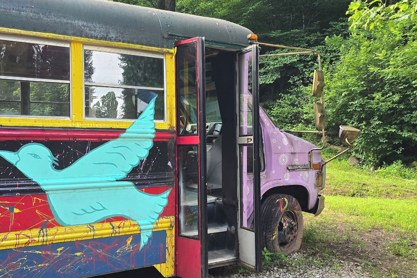 A bus with a colorful exterior and a door open, parked in a natural setting.