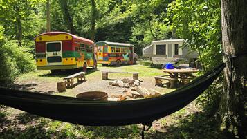 Un hamac tendu entre deux arbres, une table de pique-nique et un camping-car dans une zone boisée.