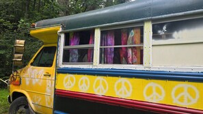 A colorful bus with a side door, large windows, and a visible interior with curtains.