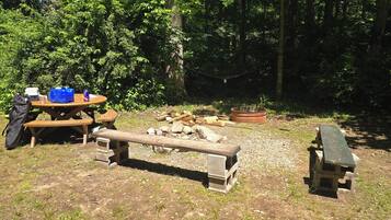 Un montaje para picnic con mesa, bancos y un hogar para fuego en una zona boscosa.