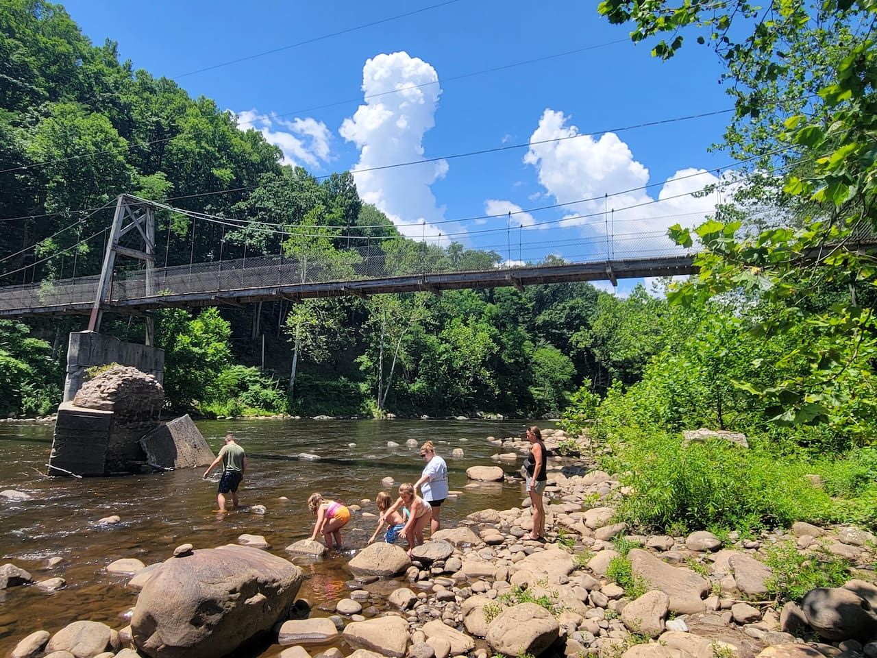 A group of people standing by a river with a bridge in the background.