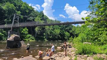 A group of people standing by a river with a bridge in the background.