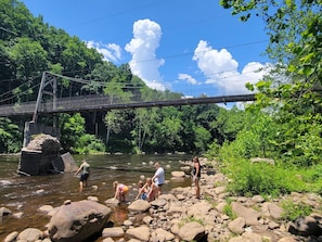 A group of people standing by a river with a bridge in the background.
