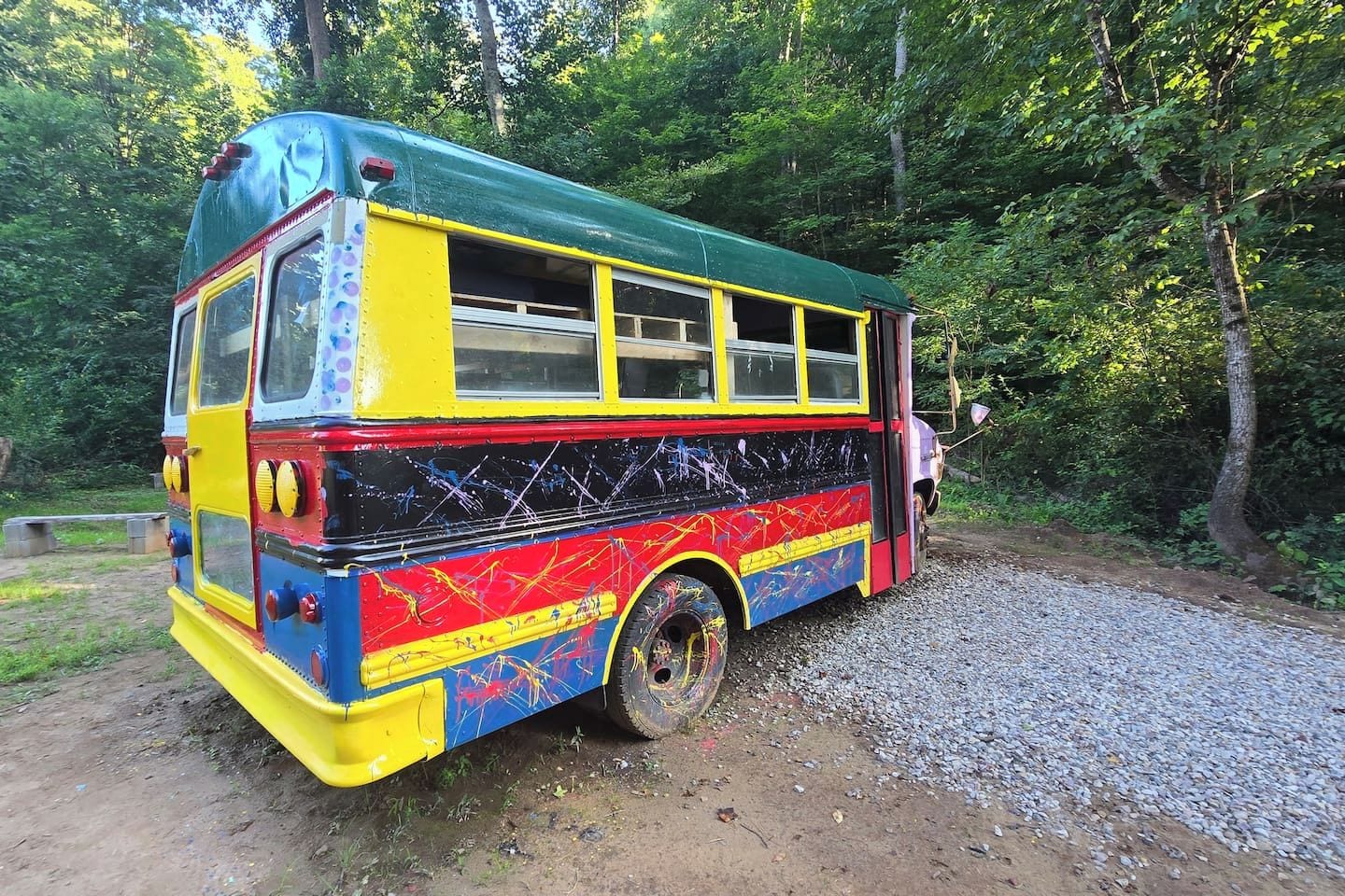 Ein farbenfroher Bus, der an einem Schotterweg inmitten von Bäumen parkt.