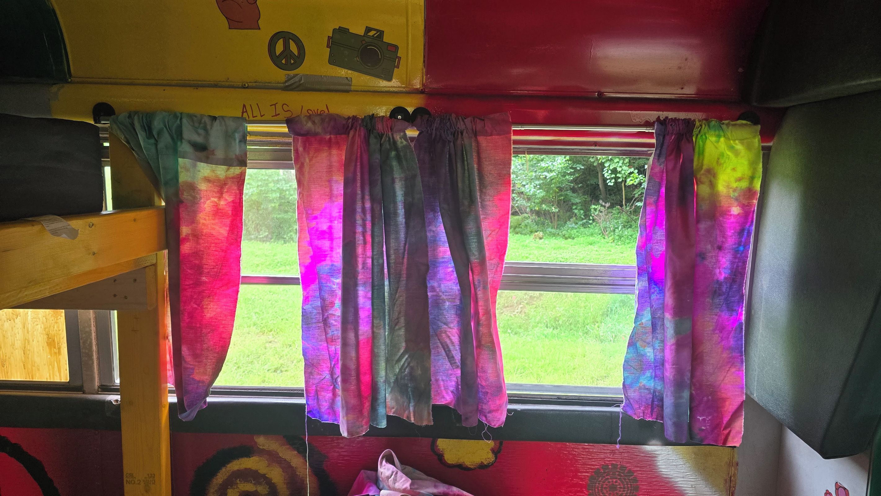 Ein Etagenbett mit Fenster, bunten Vorhängen und einem Friedenssymbol an der Wand.