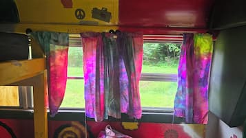 Ein Etagenbett mit Fenster, bunten Vorhängen und einem Friedenssymbol an der Wand.