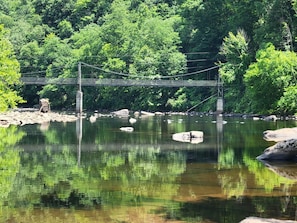 Un puente colgante sobre un río tranquilo, flanqueado por abundante vegetación a ambos lados.