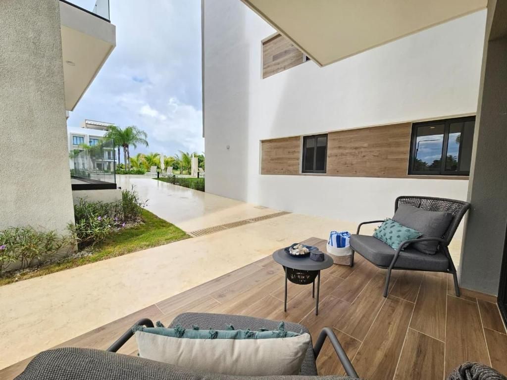 Uma área de estar moderna ao ar livre, com um sofá, cadeiras, uma pequena mesa e vista para um edifício ao fundo.
