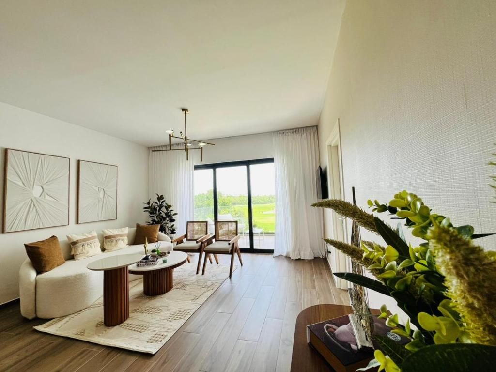 Una sala de estar moderna con sofá, mesa de centro y sillas, un ventanal con cortinas y una planta.