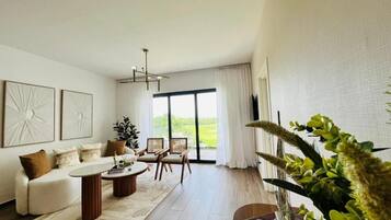 Una sala de estar moderna con sofá, mesa de centro y sillas, un ventanal con cortinas y una planta.