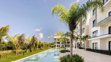 A modern hotel with a swimming pool, surrounded by palm trees and greenery.