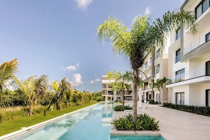 Um hotel moderno com piscina, rodeado por palmeiras e vegetação.