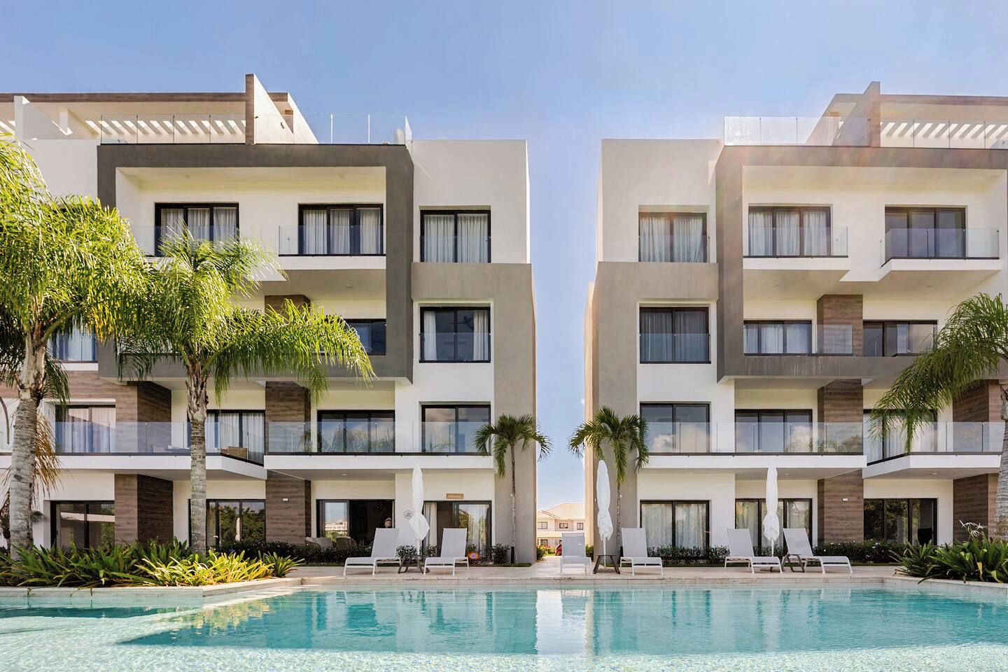 A modern hotel with a pool, multiple balconies, and palm trees.