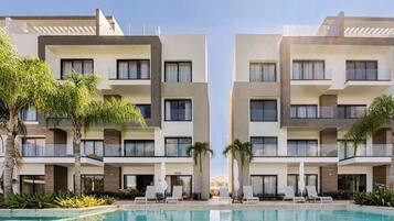 A modern hotel with a pool, multiple balconies, and palm trees.