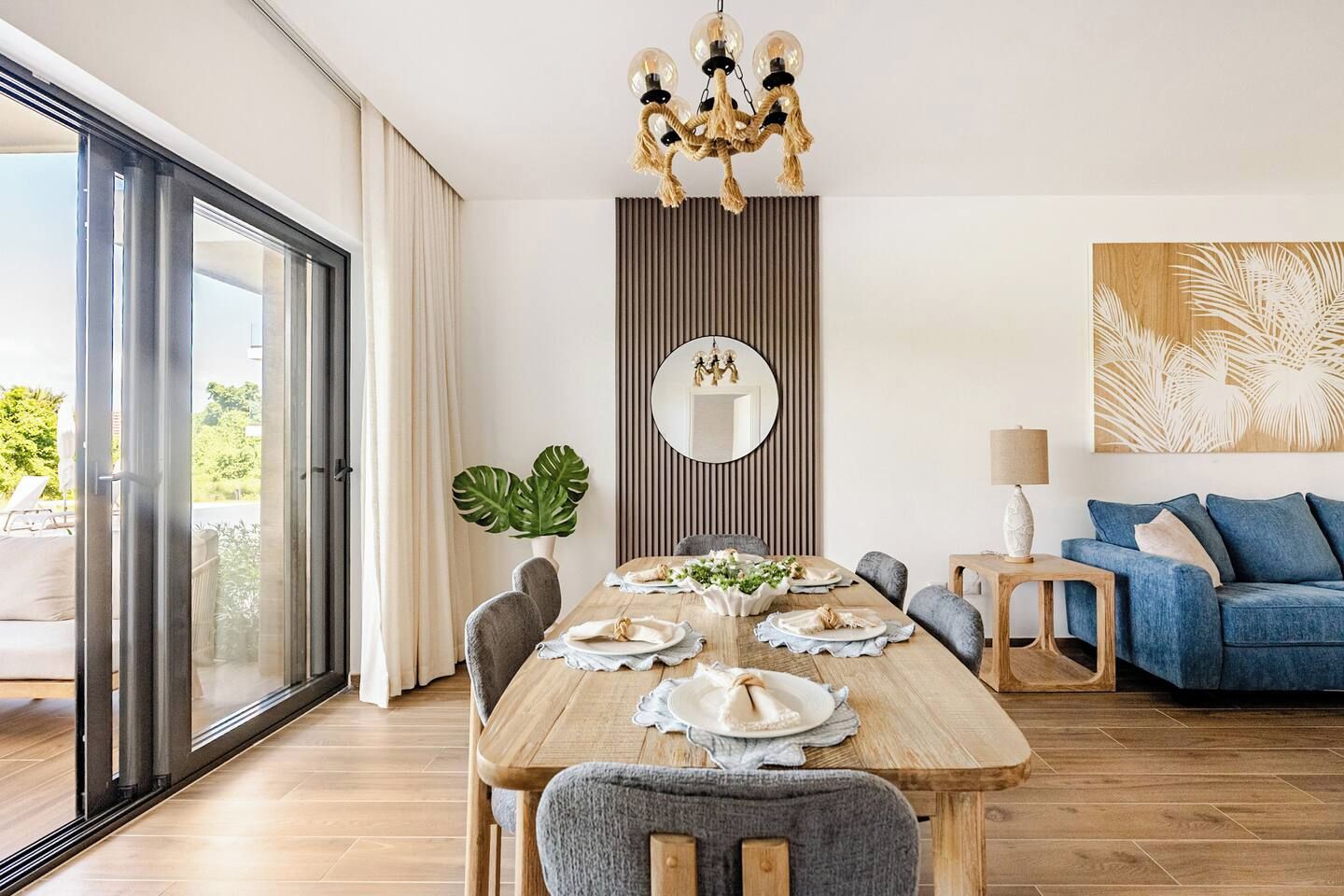 A modern dining area with a wooden table set for four, a large mirror, and a blue sofa in the background.
