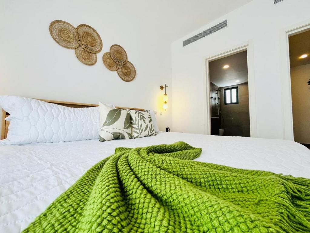 A hotel room with a bed, a green blanket, a wall-mounted light, and a door leading to another room.