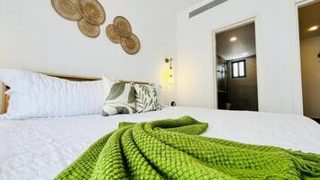 A hotel room with a bed, a green blanket, a wall-mounted light, and a door leading to another room.