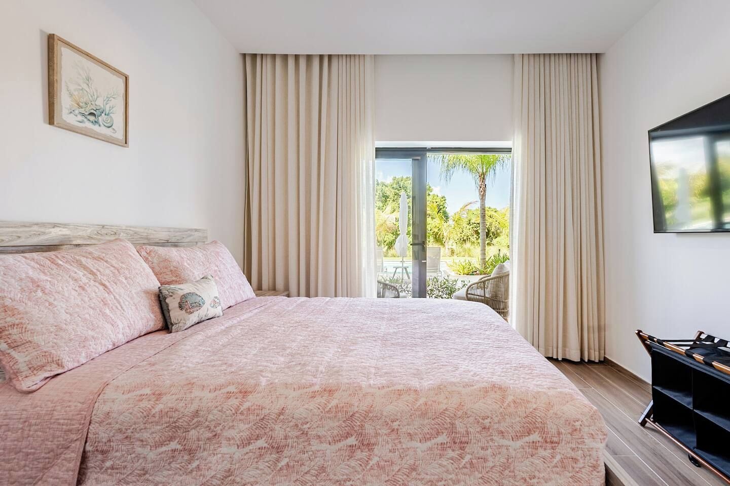 Une chambre avec un grand lit, des rideaux beiges, une télévision et une vue sur la verdure.