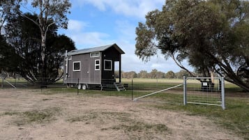 Une petite cabane à un seul étage, avec un toit en métal, entourée d’une zone délimitée par une clôture et plantée d’arbres.