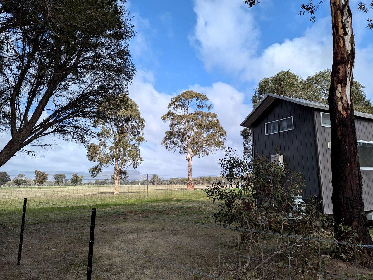 A fenced property with a building, trees, and a clear sky.