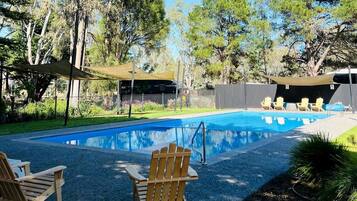 A swimming pool with a wooden deck, surrounded by trees and a covered seating area.