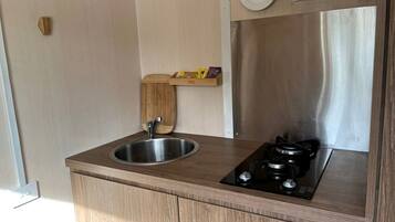 Een kleine keuken met een roestvrijstalen spoelbak, een zwart fornuis en houten keukenkastjes.
