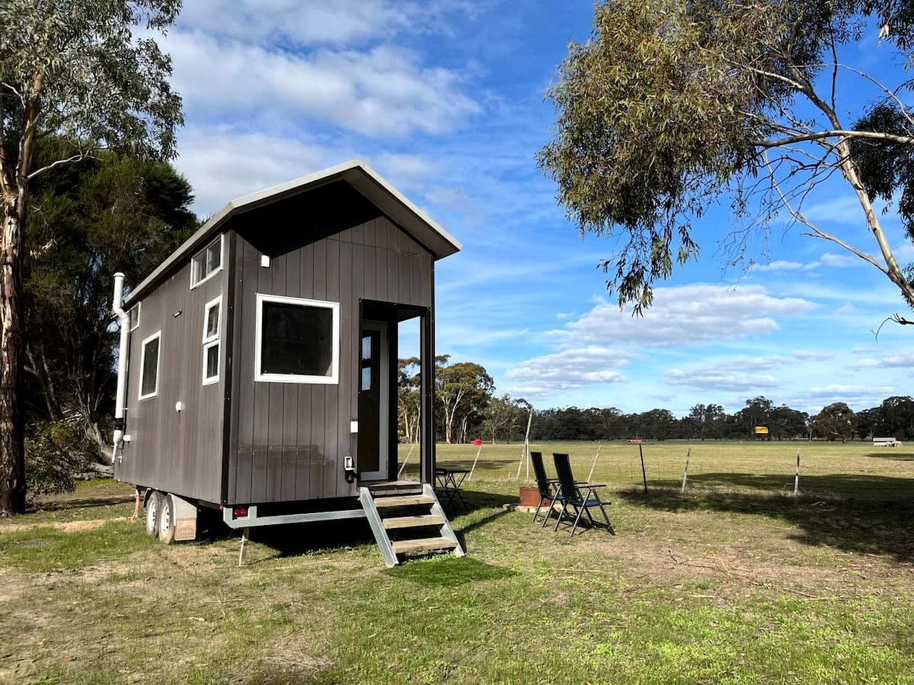 A small, single-story cabin with a door and windows, situated on a grassy area with trees in the background.