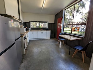 Eine kleine Küche mit Kühlschrank, Schränken, einer Spüle und einem Fenster mit Blick auf einen Garten.