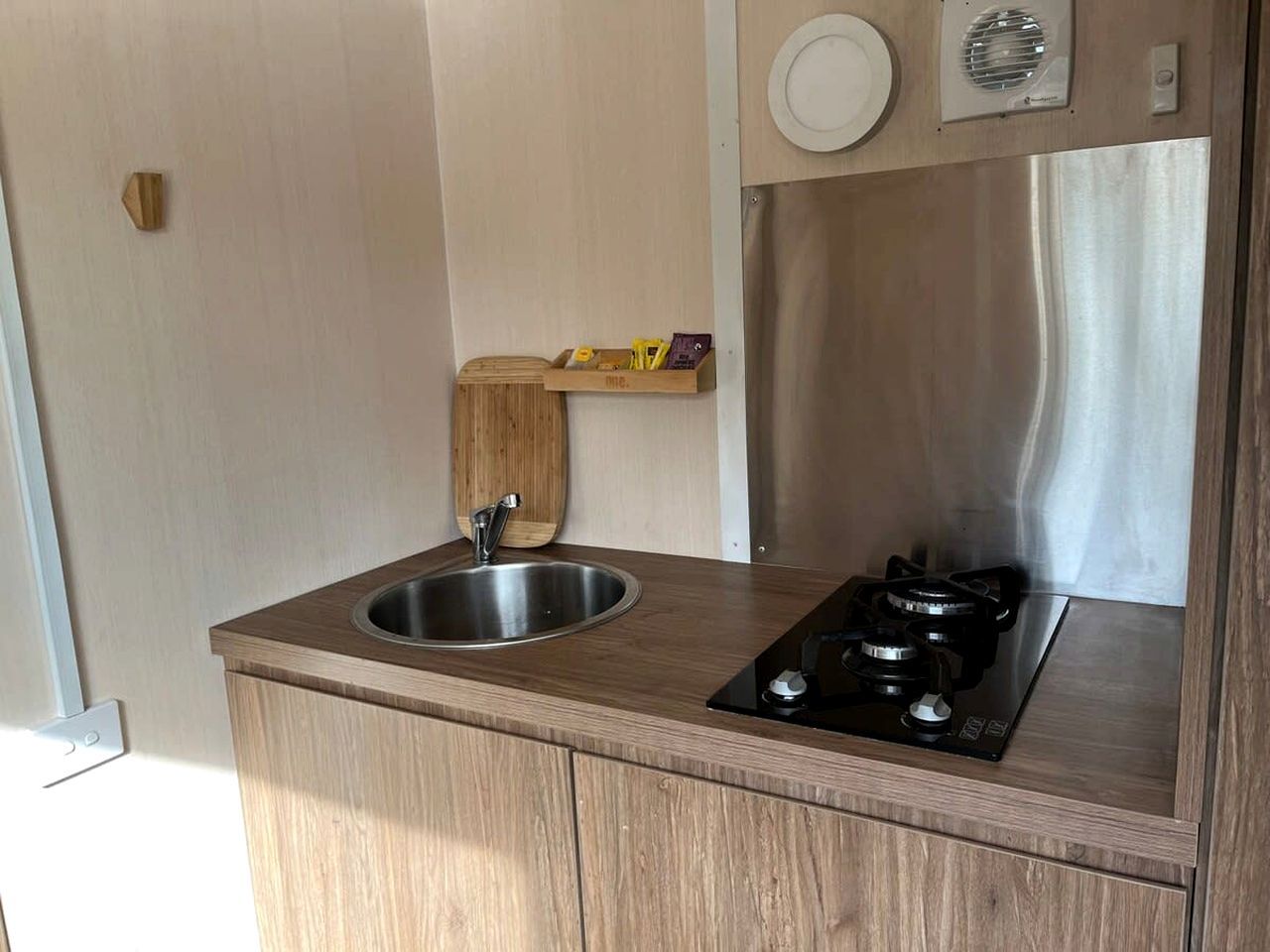 Una cocina compacta con un lavamanos de acero inoxidable, una estufa negra y armarios de madera.