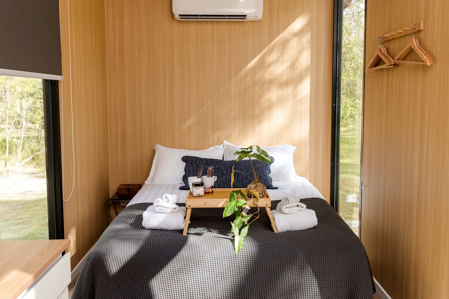 A modern bedroom with a bed, pillows, a tray with towels, a plant, and a wooden hanger.
