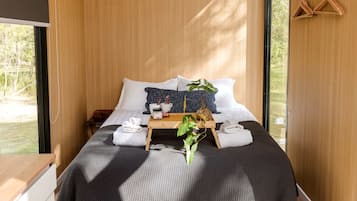 A modern bedroom with a bed, pillows, a tray with towels, a plant, and a wooden hanger.