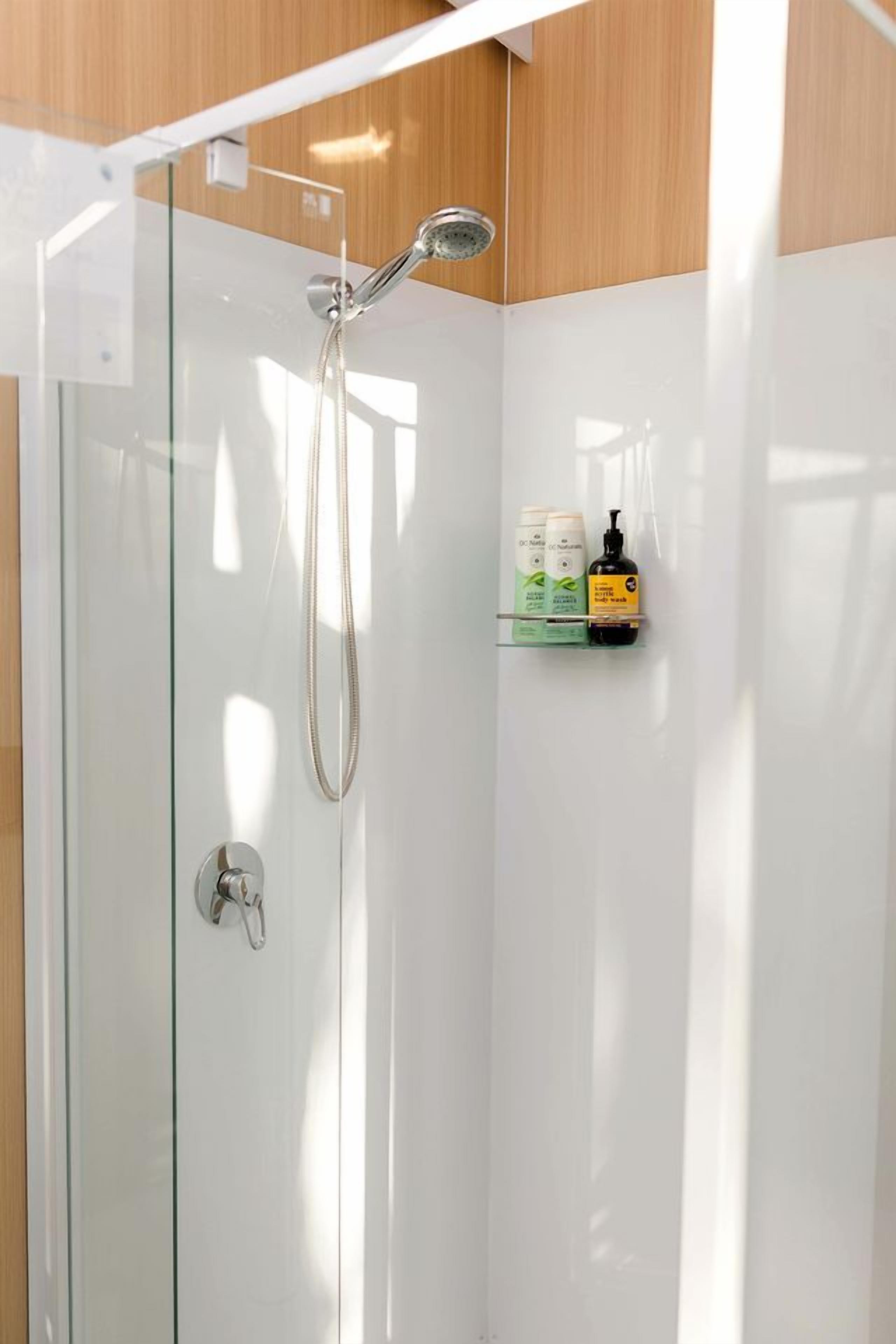 A glass-enclosed shower with a handheld showerhead and a wall-mounted faucet.