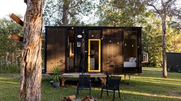 A modern cabin with a large sliding door, a dining area with a table and chairs, and a visible bedroom with a bed.