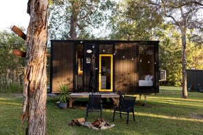 A modern cabin with a large sliding door, a dining area with a table and chairs, and a visible bedroom with a bed.