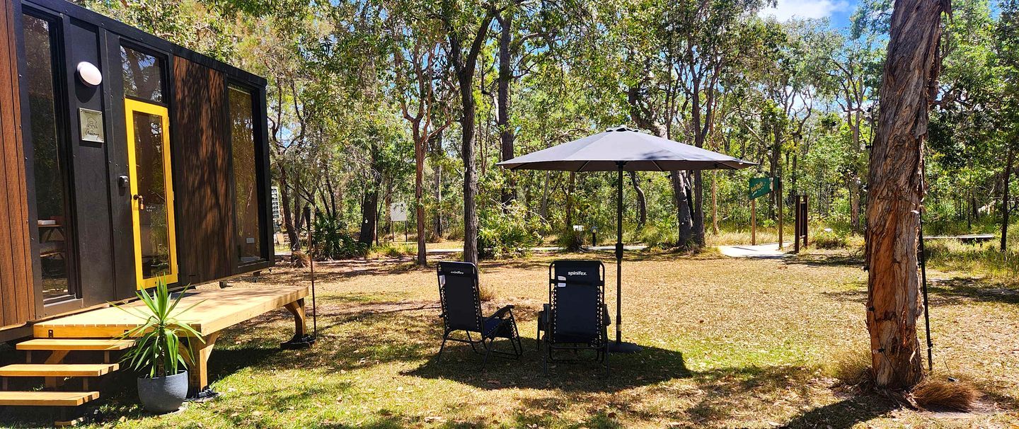 Una estructura de madera con una puerta amarilla, una mesa de picnic y dos sillas.