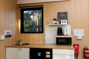 A compact kitchen with a sink, a microwave, a coffee maker, and a fire extinguisher.