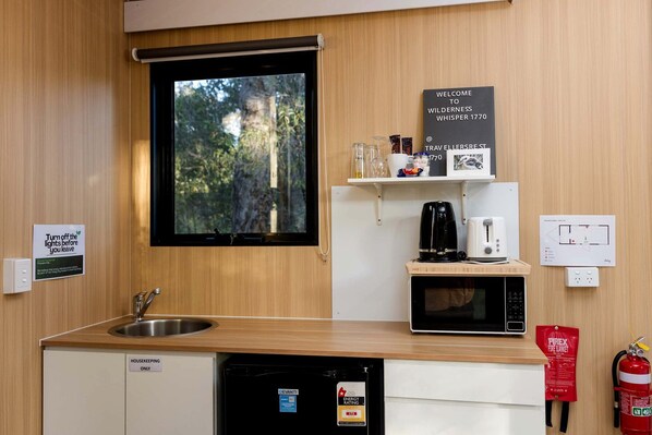 A compact kitchen with a sink, a microwave, a coffee maker, and a fire extinguisher.