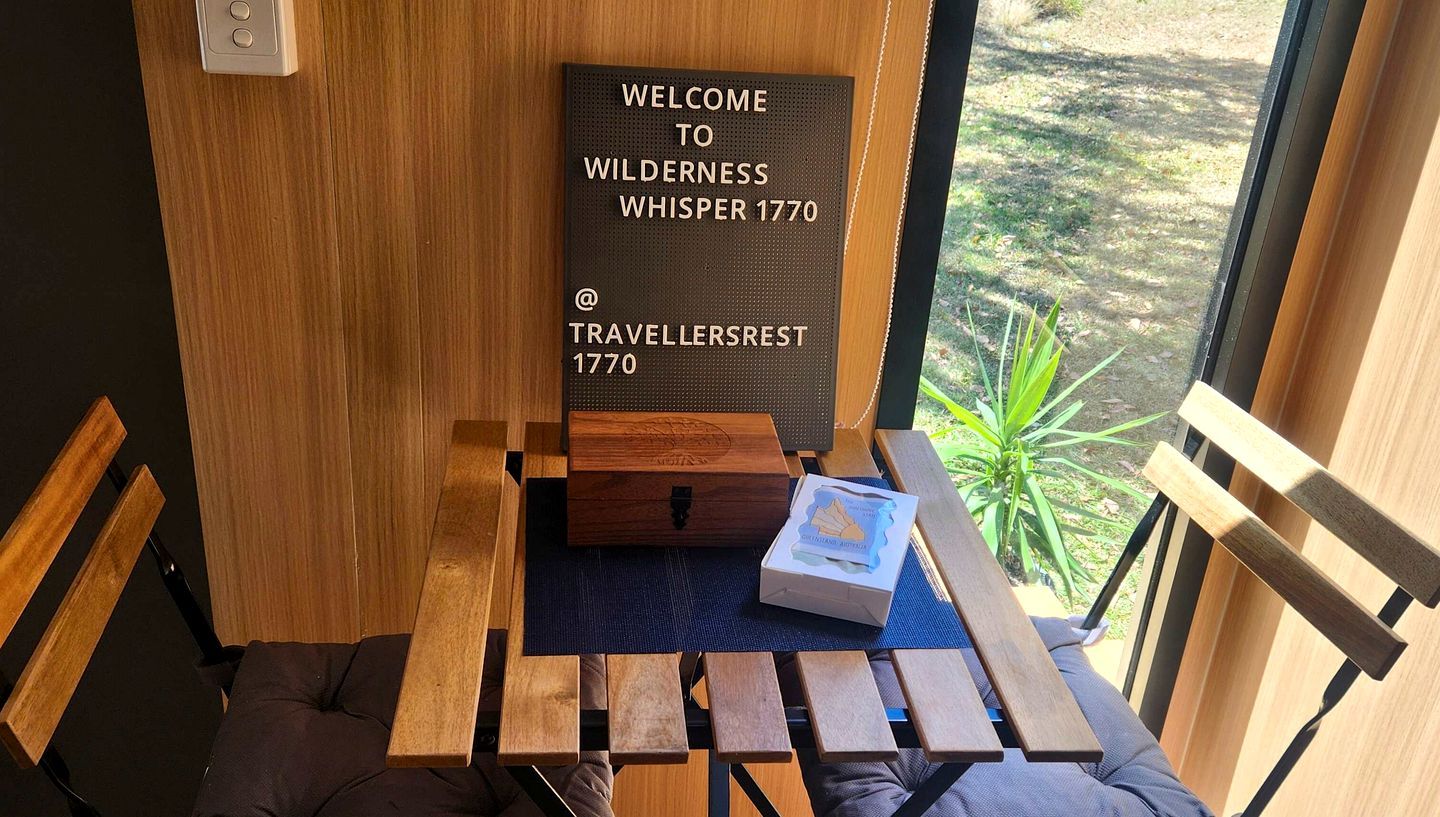 A wooden bench with a small table, a welcome sign, and a box on the table.