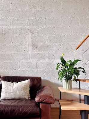 Ein Zimmer mit einem braunen Ledersofa, einem weißen Kissen, einem Holztisch und einer Blumentopf-Pflanze.