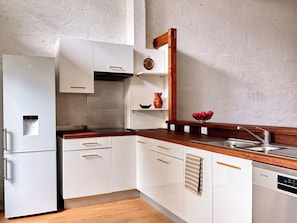 Eine kompakte Küche mit weißen Schränken, einer Holz Arbeitsplatte, einem eingebauten Backofen und einem Geschirrspüler.